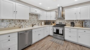 A modern kitchen with white cabinets, a stainless steel dishwasher, a microwave, a stove, and a coffee maker.