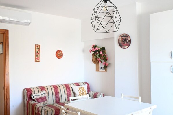 A dining area with a white table and chairs, a striped sofa, and a geometric pendant light.