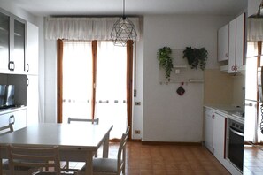 A kitchen with a dining table, chairs, cabinets, a stove, and hanging plants.