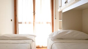A bedroom with two beds, a wooden door, and a window with sheer curtains. - M033 - Marcelli, three-room apartment in the center facing the sea (Marcelli)