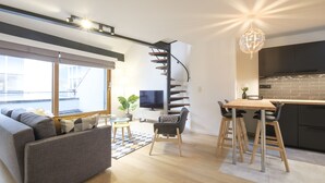 Ett modernt vardagsrum med en soffa, en matplats med bord och stolar, en TV och en trappa.