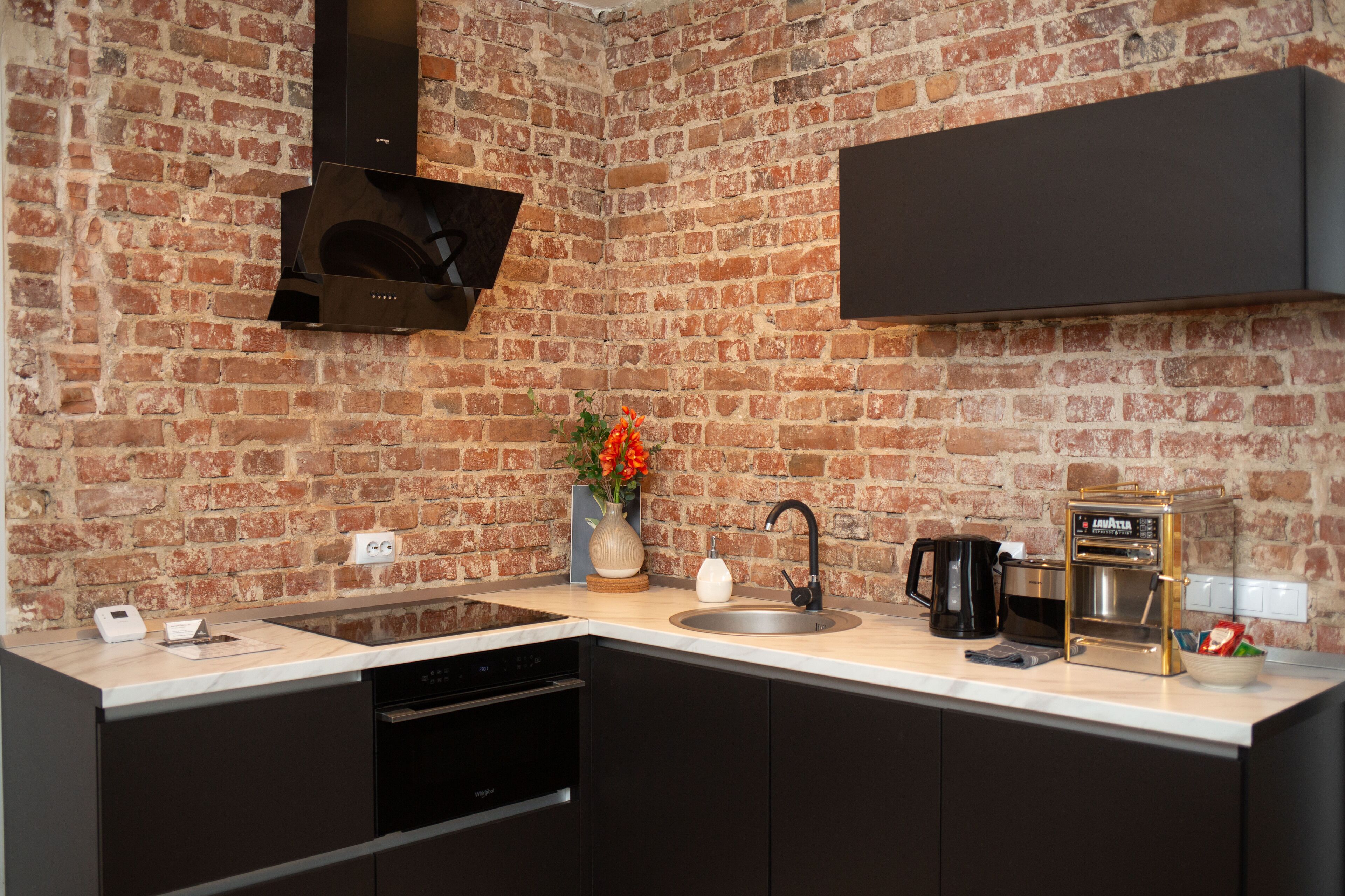 A kitchen with a brick wall, a modern stove, a sink, and a coffee machine.