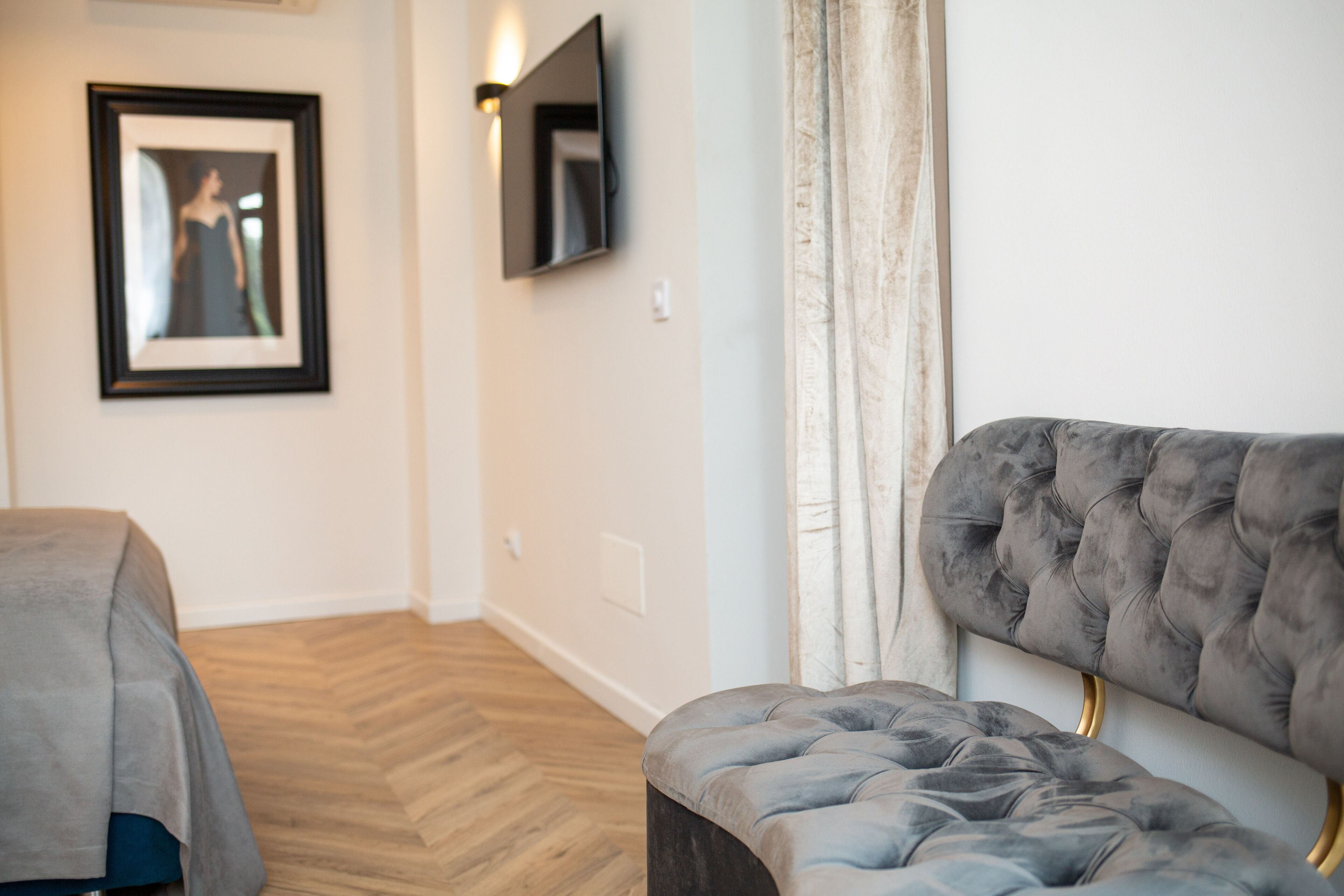 Una habitación moderna con cabecera capitonada, un cuadro enmarcado en la pared y un televisor de pantalla plana montado sobre un suelo de madera.