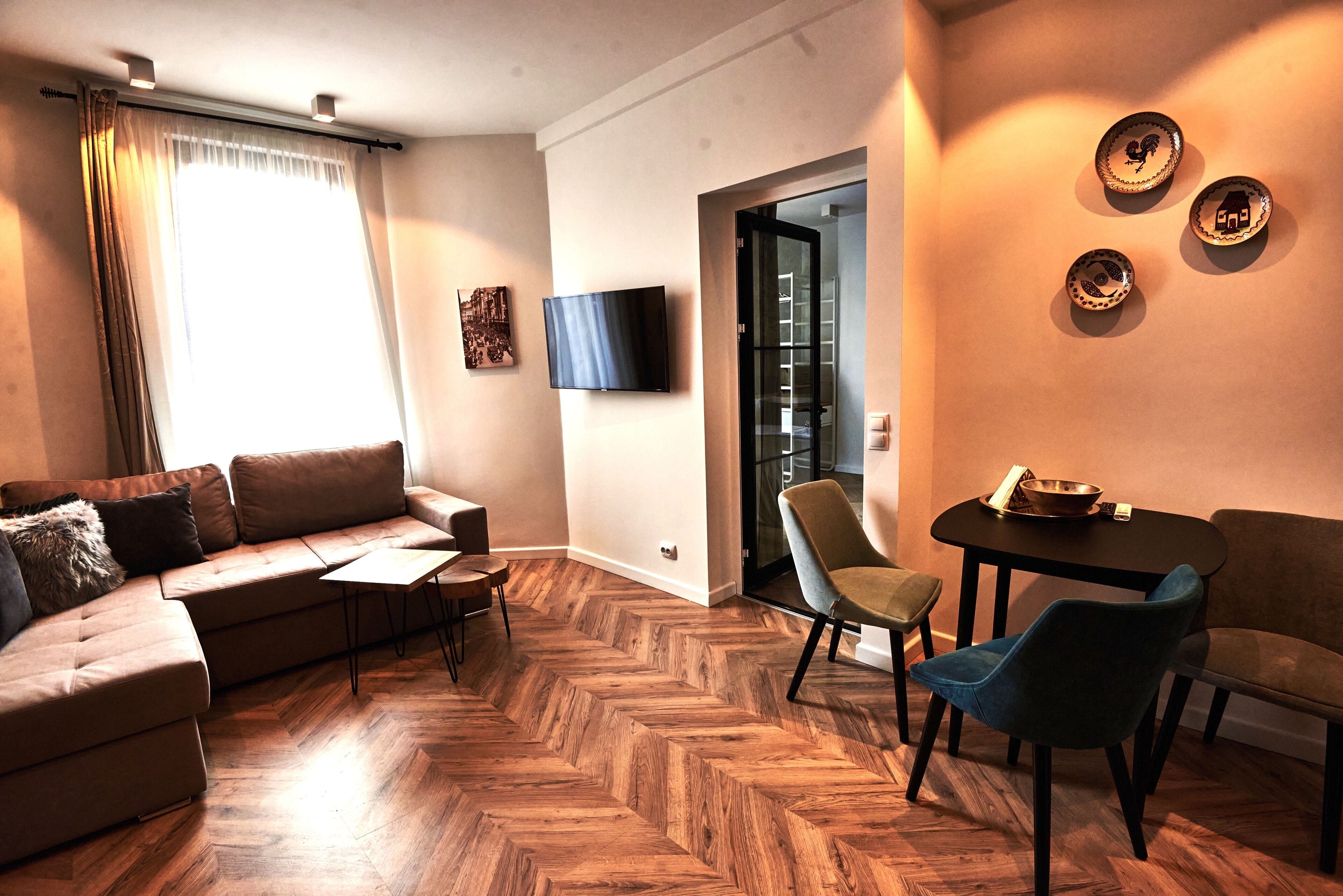 A modern living room with a herringbone wood floor, a sofa, a TV, and a dining area with chairs and a table.