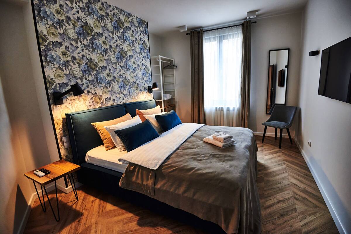 A modern hotel room with a large bed, a nightstand, a wall-mounted TV, and a mirror.
