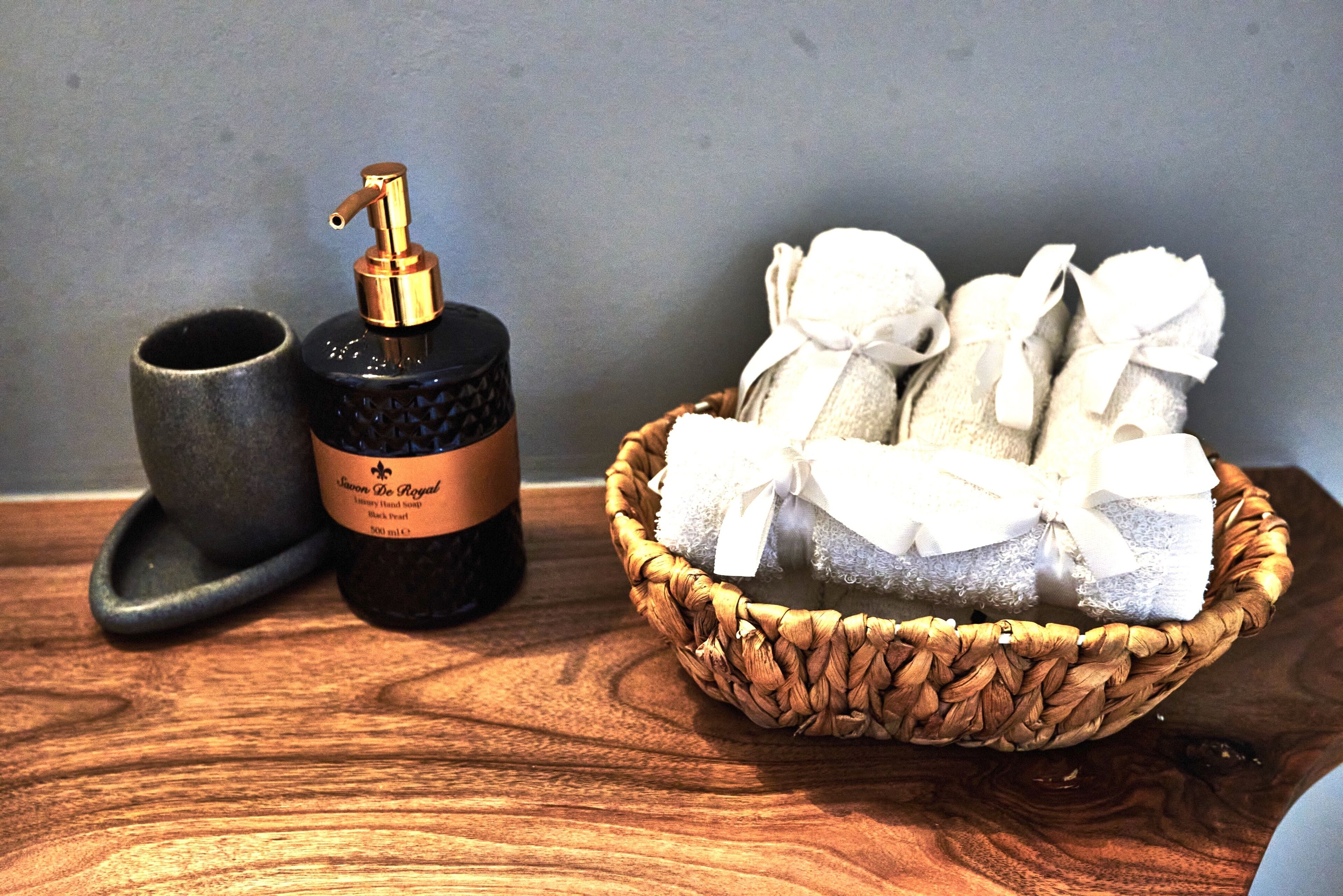Una mesa de madera con una botella negra, una taza de cerámica y una cesta de toallas blancas.