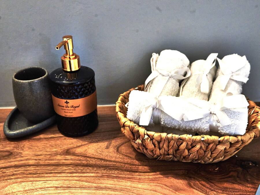 Una mesa de madera con una botella negra, una taza de cerámica y una cesta de toallas blancas.