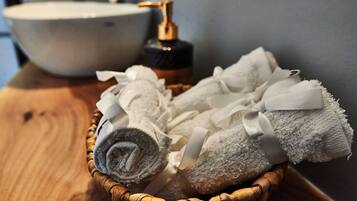 A wooden table with a wicker basket containing rolled towels and a bottle of liquid soap.