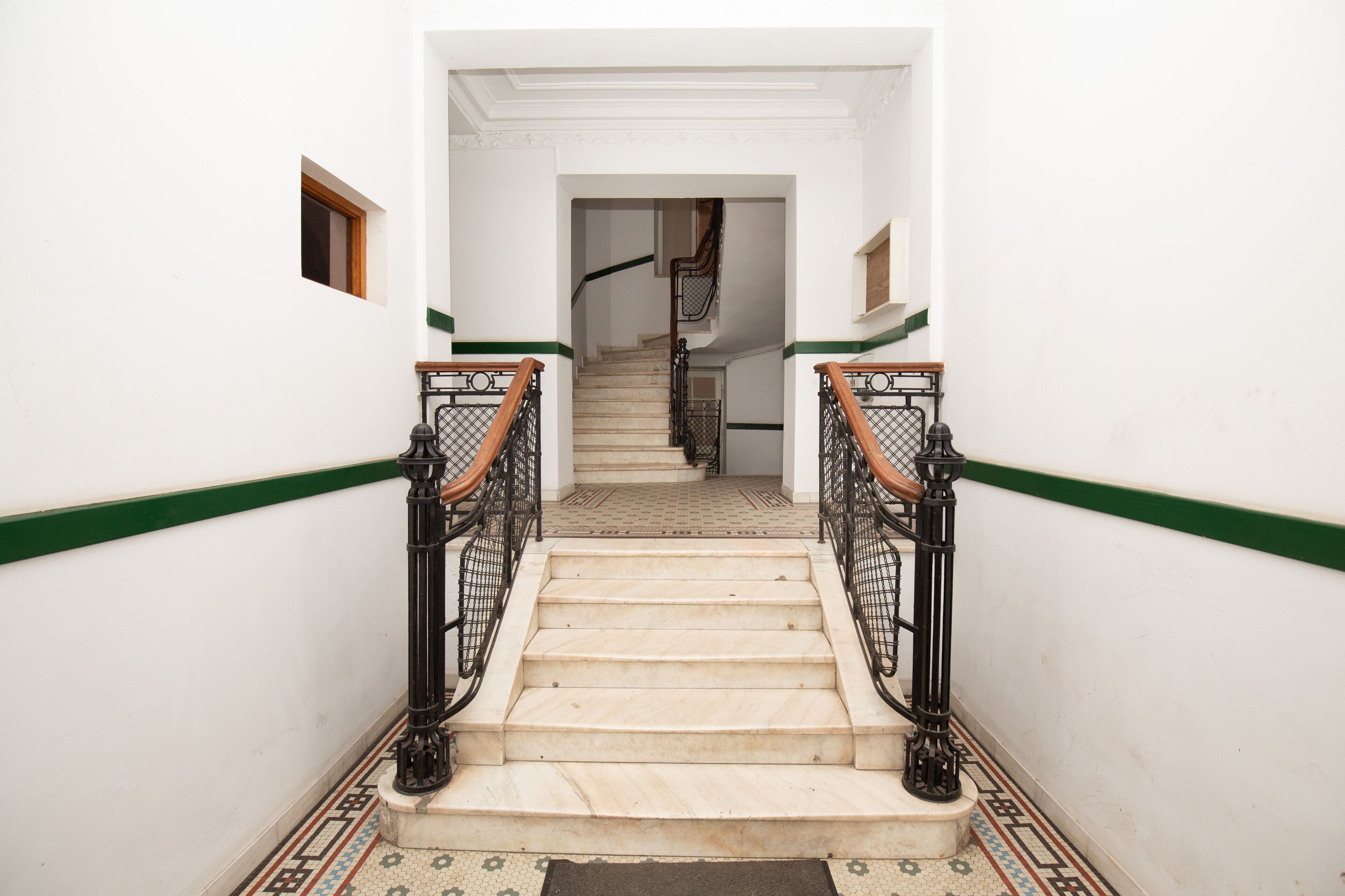 A staircase with a green stripe, black railings, and patterned floor tiles.