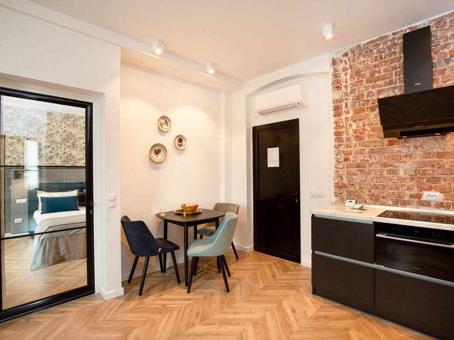 Una cocina moderna con pared de ladrillo, una zona de comedor con dos sillas y una mesa, y un lavavajillas negro.