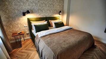 Een net opgemaakt bed met een groen hoofdbord, twee bedlampjes en een houten nachtkastje met een afstandsbediening.