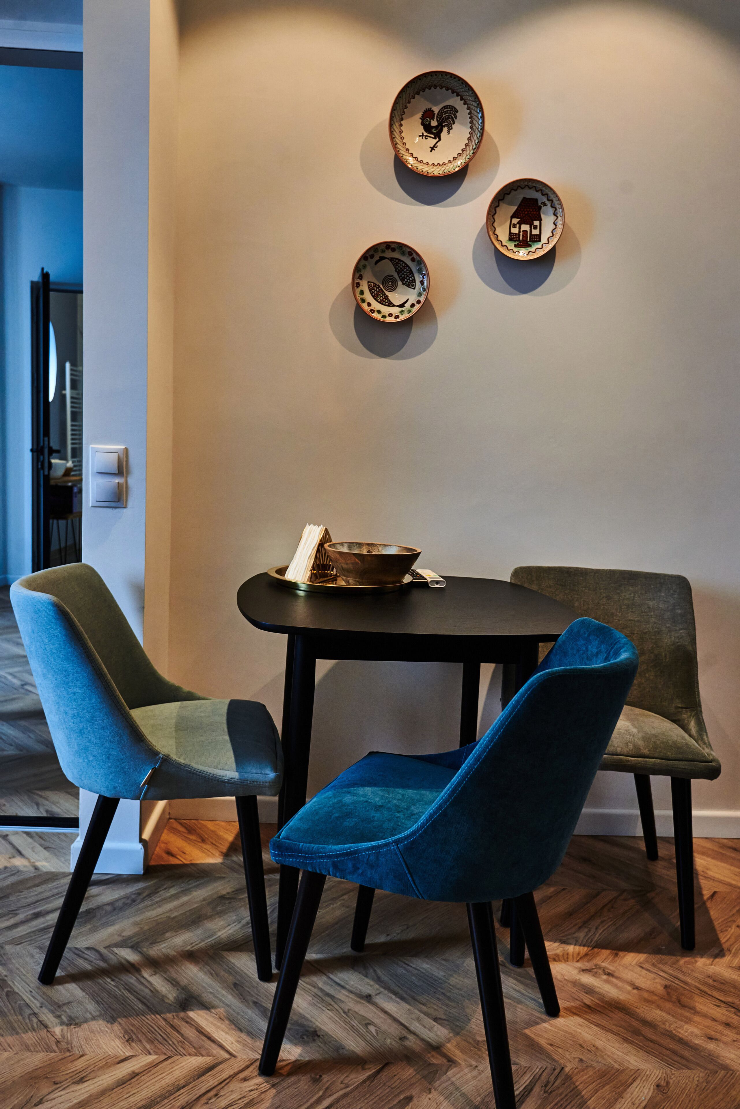 A dining area with a table and four chairs, a wall-mounted light fixture, and a door in the background.