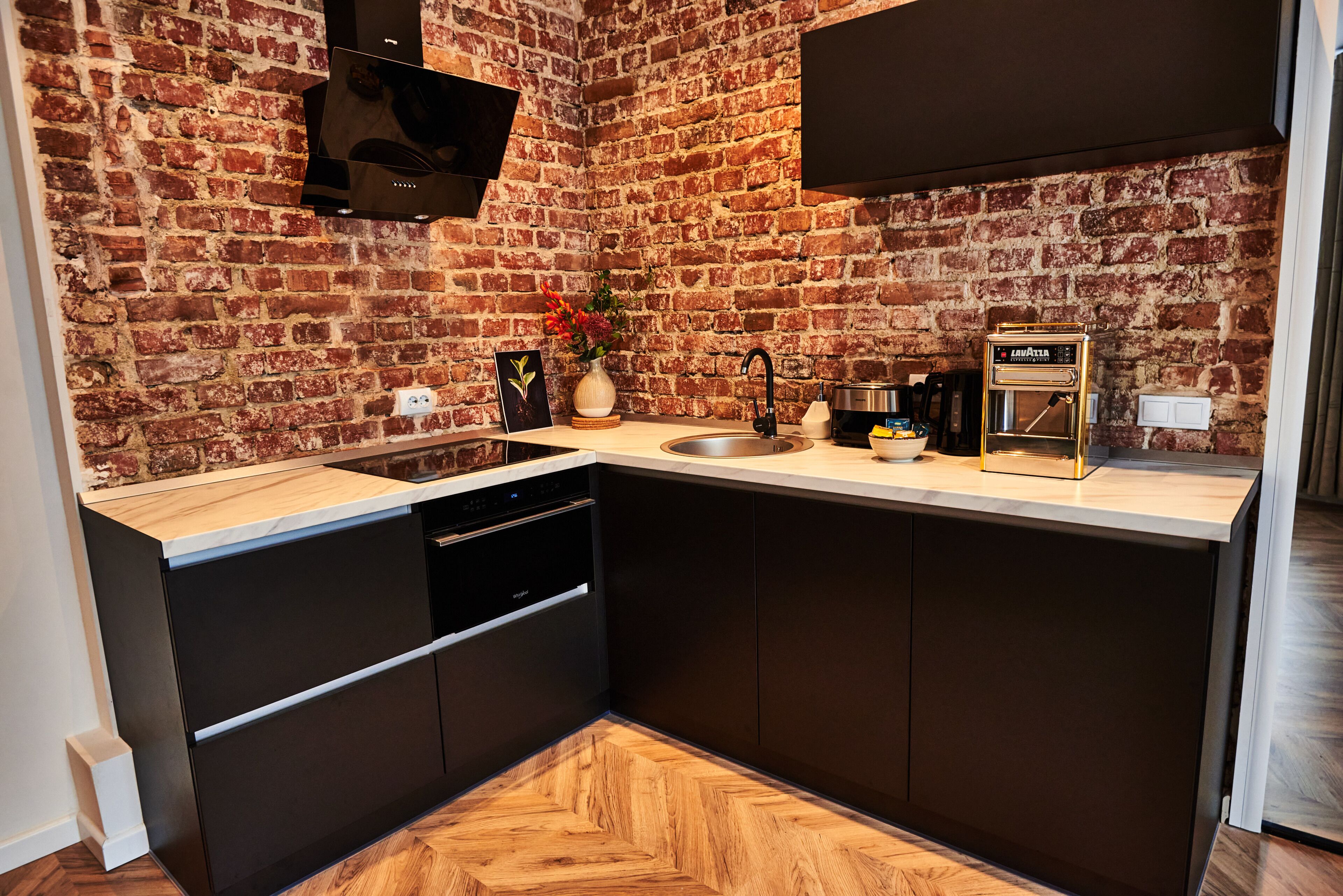 A modern kitchen with a brick wall, a built-in dishwasher, and a coffee machine.