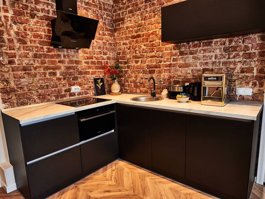 A modern kitchen with a brick wall, a built-in dishwasher, and a coffee machine.