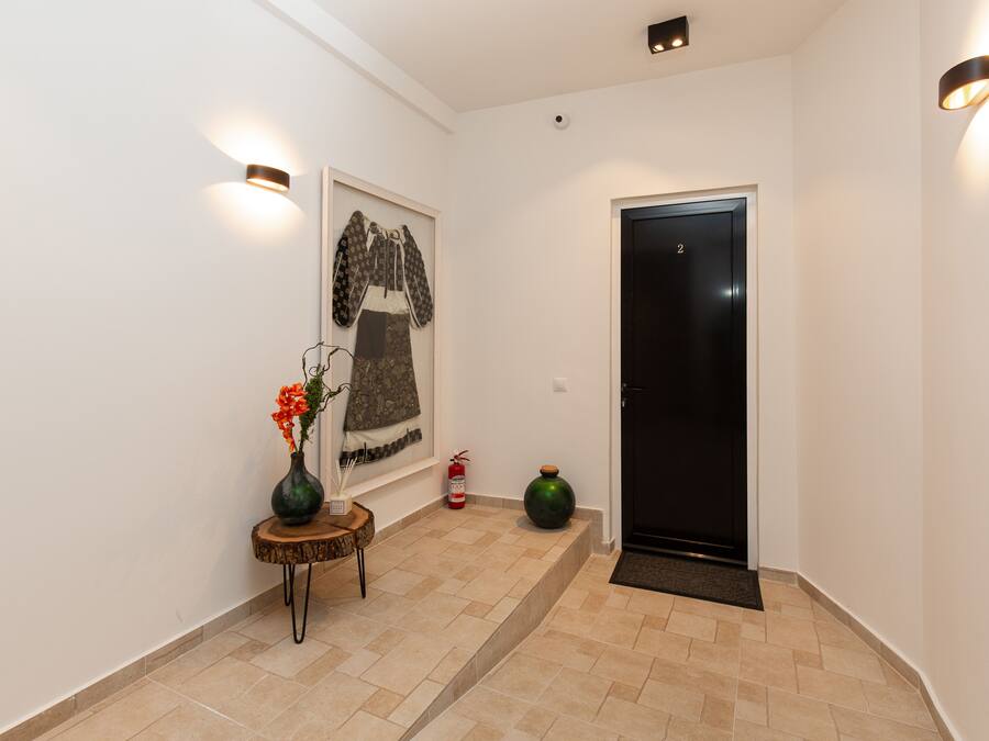 A hallway with a framed artwork, a small table with a vase, a fire extinguisher, and a door.
