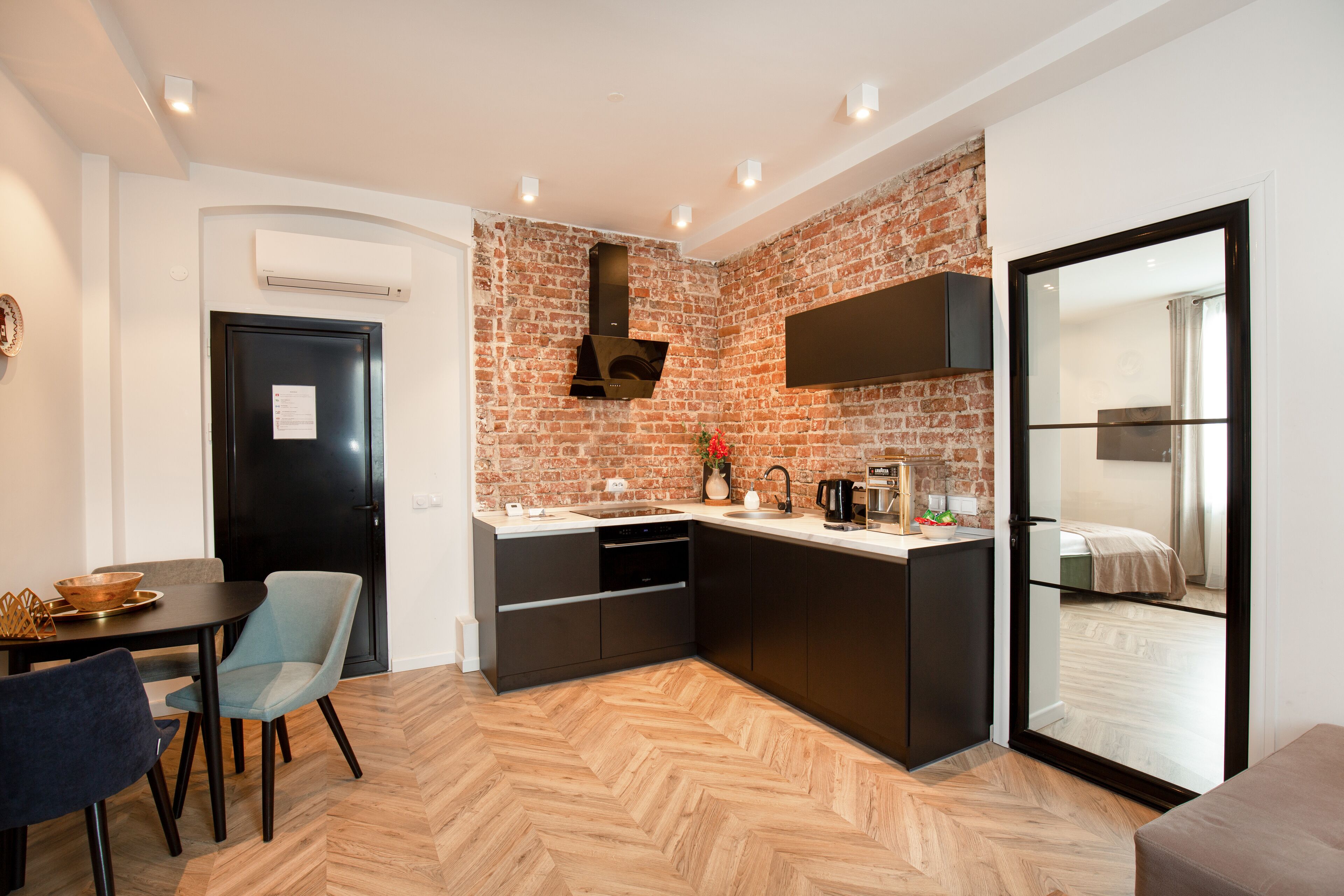 A compact kitchen with a herringbone wood floor, a black refrigerator, and a built-in oven.