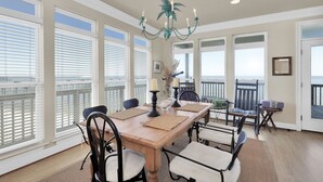 A dining area with a wooden table, chairs, and a chandelier. There are large windows with blinds and a view of the ocean. - Corner pet-friendly, 5/3 bay sunset views! - TraMarLis (Dauphin Island)