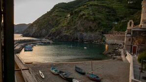 A coastal scene with boats docked at a pier, a rocky hillside, and a building with a balcony overlooking the water. - Vernazza Sea View (Vernazza)