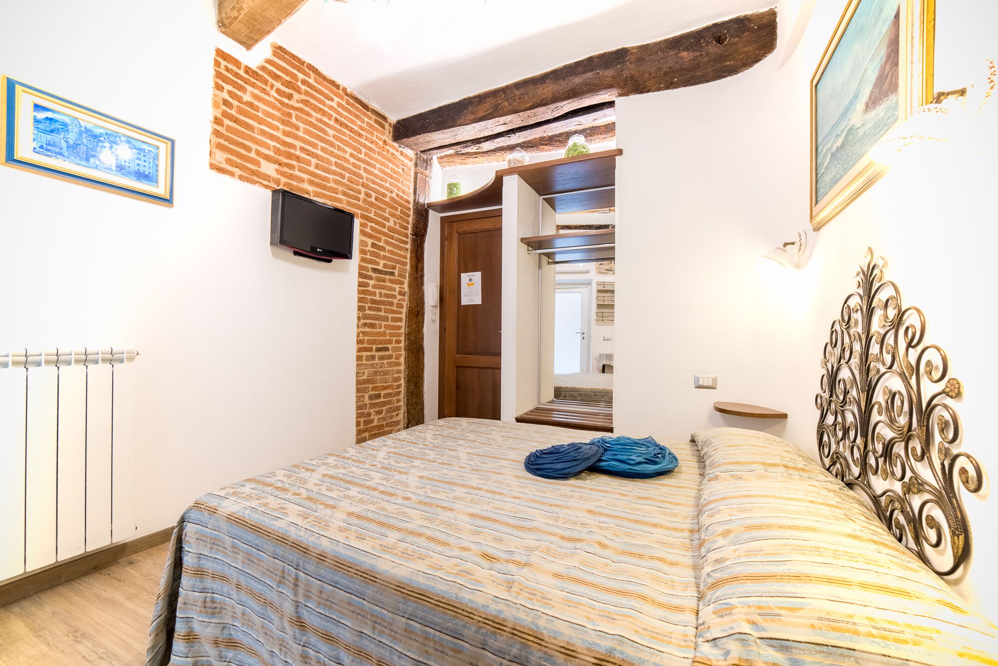 A bedroom with a brick wall, a bed with striped bedding, a TV, and a decorative headboard.