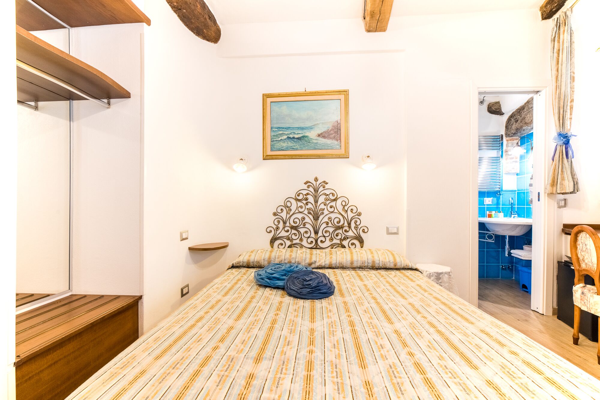 A bedroom with a bed, a headboard, a painting, and a bathroom visible through an open door.