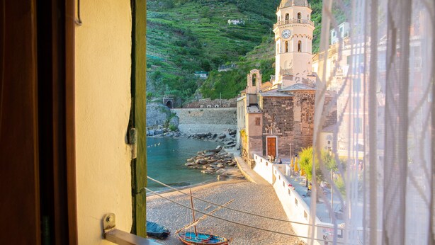 A coastal town with a prominent church tower, a rocky shoreline, and boats docked near the water. - Vernazza Sea View (Vernazza)