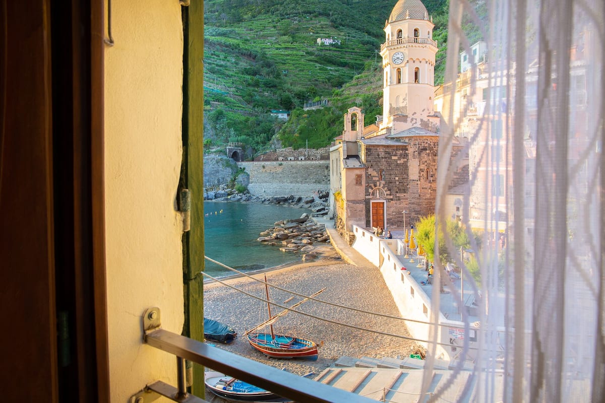 A coastal town with a prominent church tower, a rocky shoreline, and boats docked near the water.