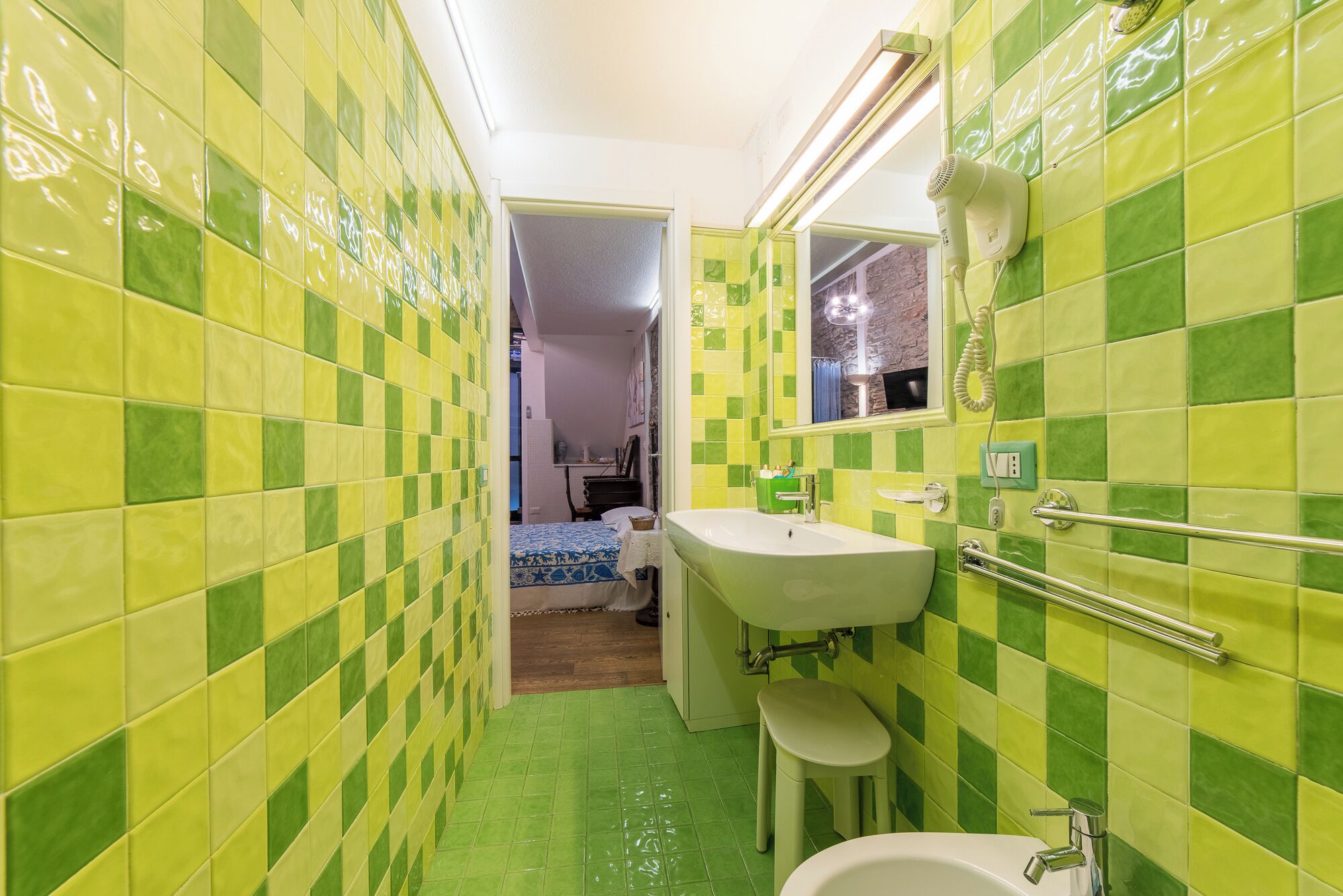 Une salle de bain avec des carreaux verts et jaunes formant un motif à carreaux, un lavabo blanc avec un miroir et un espace douche.