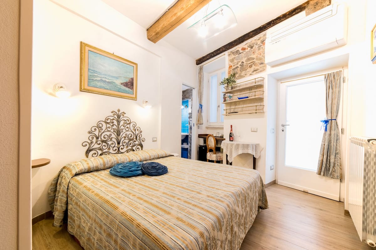A bedroom with a bed, a painting, a wooden ceiling, a door, and a window.