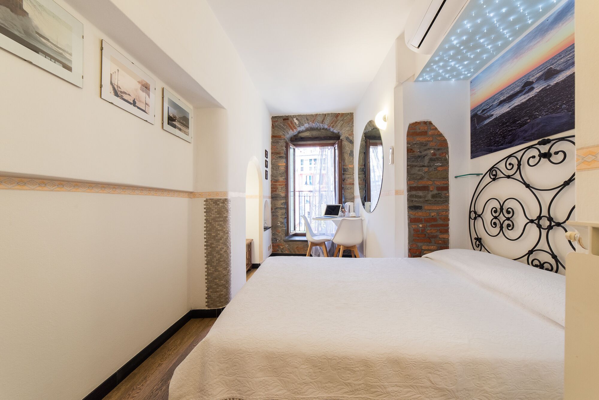 Habitación de hotel con cama, escritorio con una computadora portátil, ventana con vistas y un cuadro en la pared.