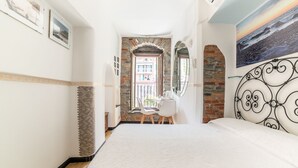 A bedroom with a large bed, a desk, and a chair, a view of a building through an open door, and a painting on the wall. - Vernazza Sea View (Vernazza)