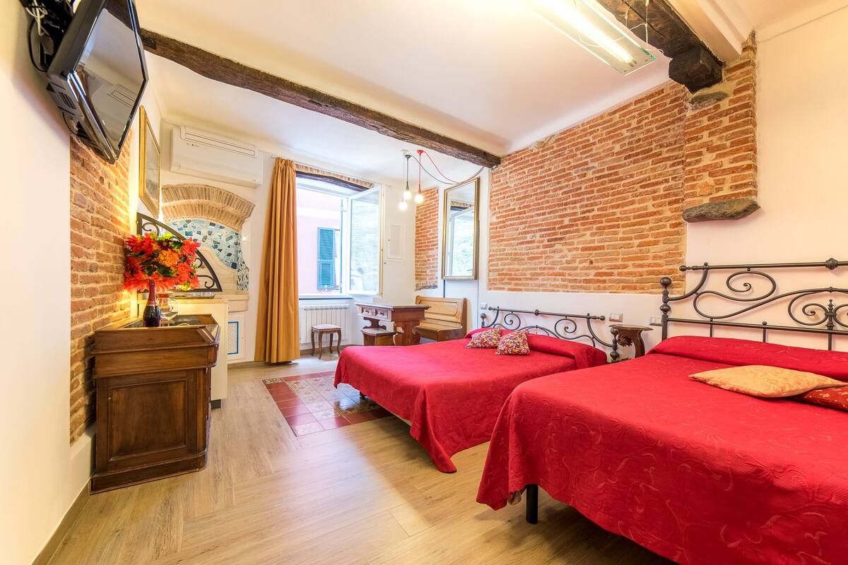 A room with two beds, a wooden dresser, a mirror, and a brick wall.
