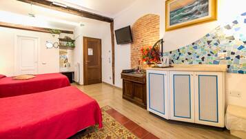 A hotel room with two beds, a small kitchenette, a TV, and a mosaic wall.
