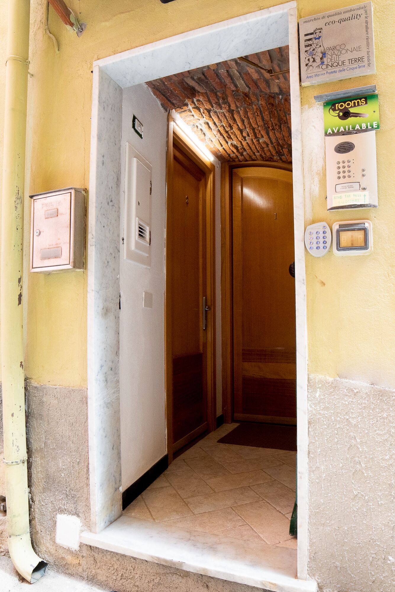 A hallway leading to a wooden door with a keypad and a card reader, a mailbox, and a sign indicating rooms are available.