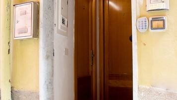 A hallway leading to a wooden door with a keypad and a card reader, a mailbox, and a sign indicating rooms are available.