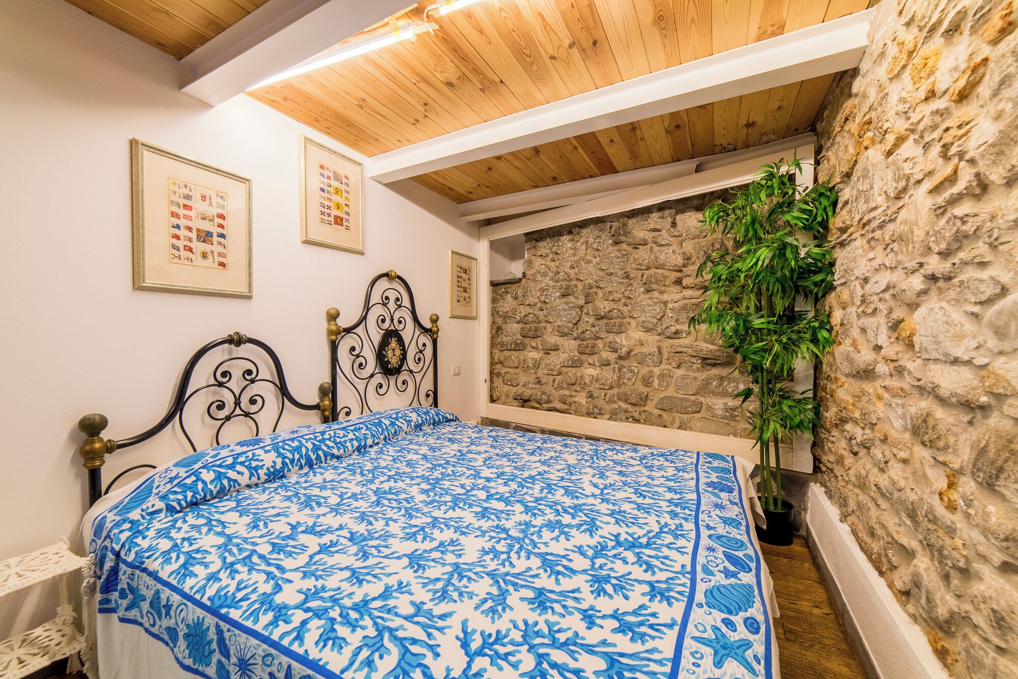 A bedroom with a bed, a stone wall, and a wooden ceiling.