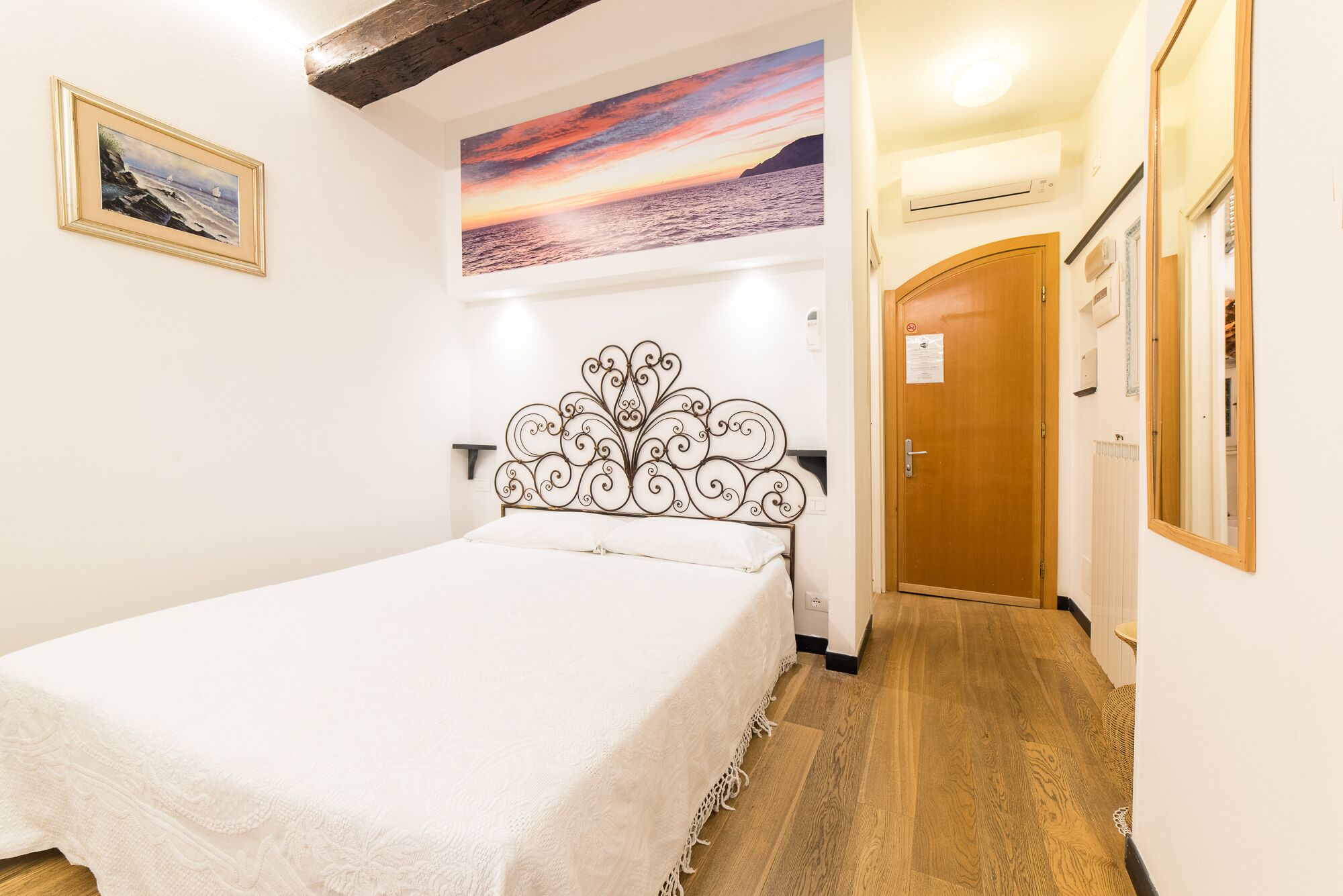 Une chambre à coucher avec un lit, un tableau représentant un coucher de soleil et une porte en bois.