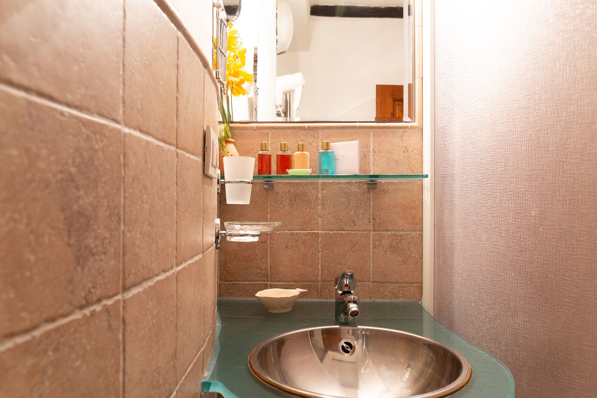 A bathroom with a round sink, a mirror, and a shelf with toiletries.