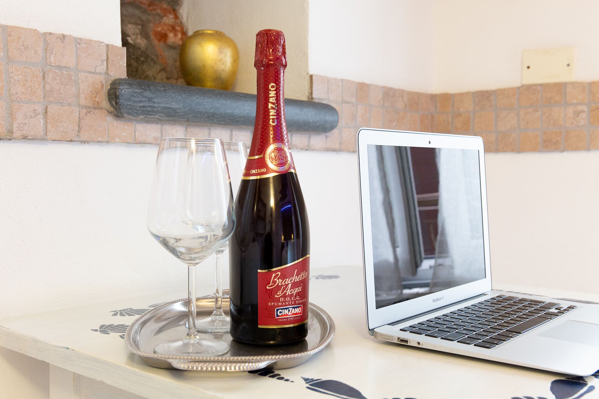 A laptop on a table with a bottle of wine and glasses.