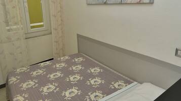 A bedroom with a bed, a nightstand, a window with curtains, and a wall-mounted painting.