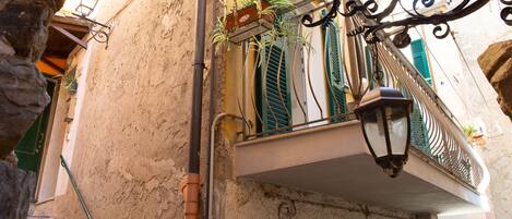 Een smalle straat met een gebouw voorzien van een balkon met groene luiken, een balkonhek van smeedijzer en een hangende lantaarn.
