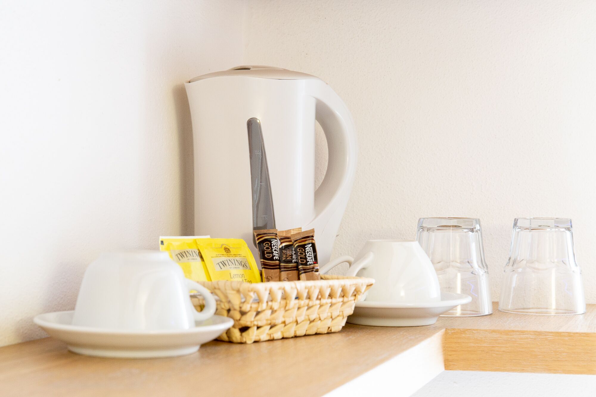 Una colazione preparata con una macchina del caffè, tazze, un cestino di bustine di tè e bicchieri.
