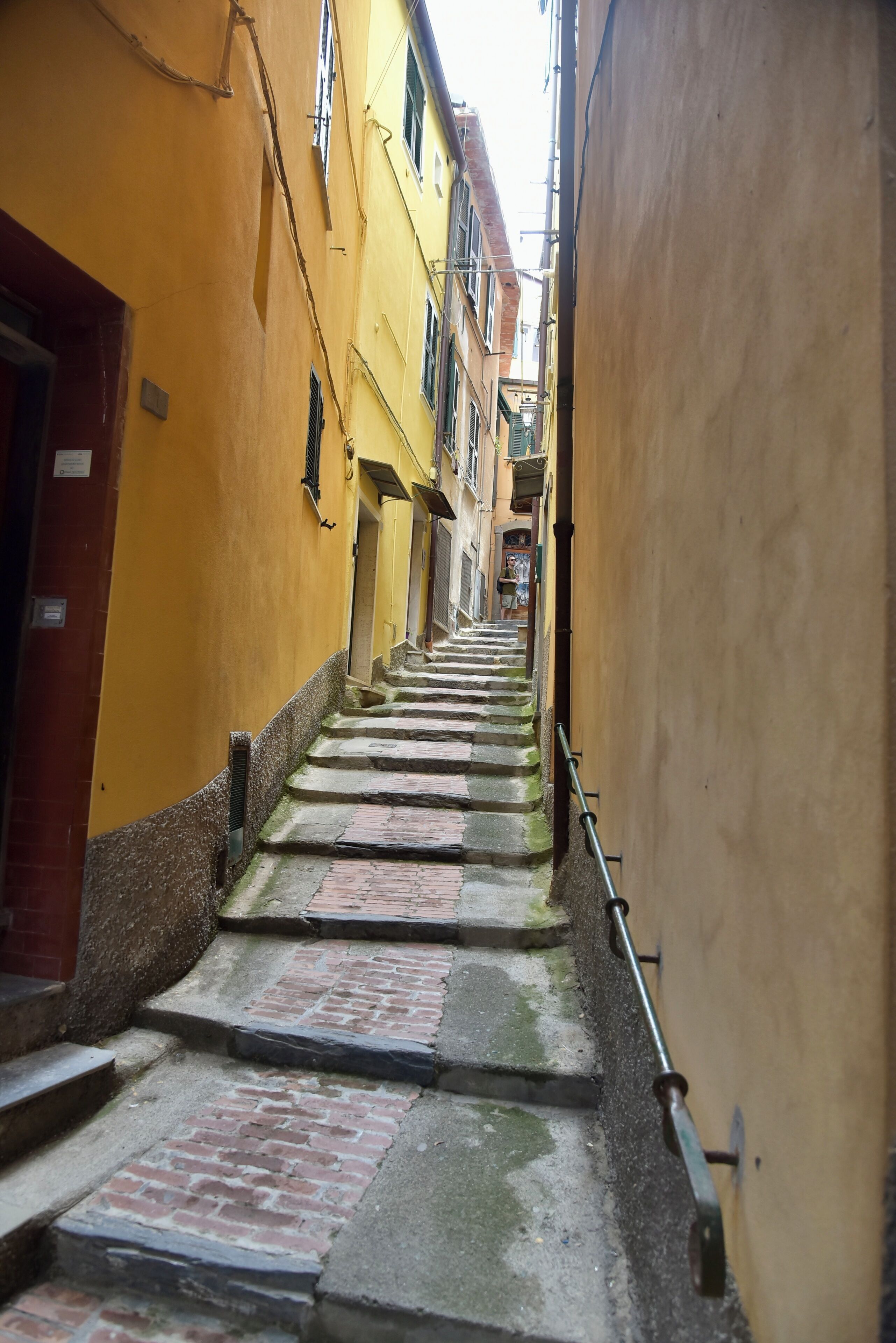 A narrow alleyway with a staircase leading up to a building with yellow walls and a red door.