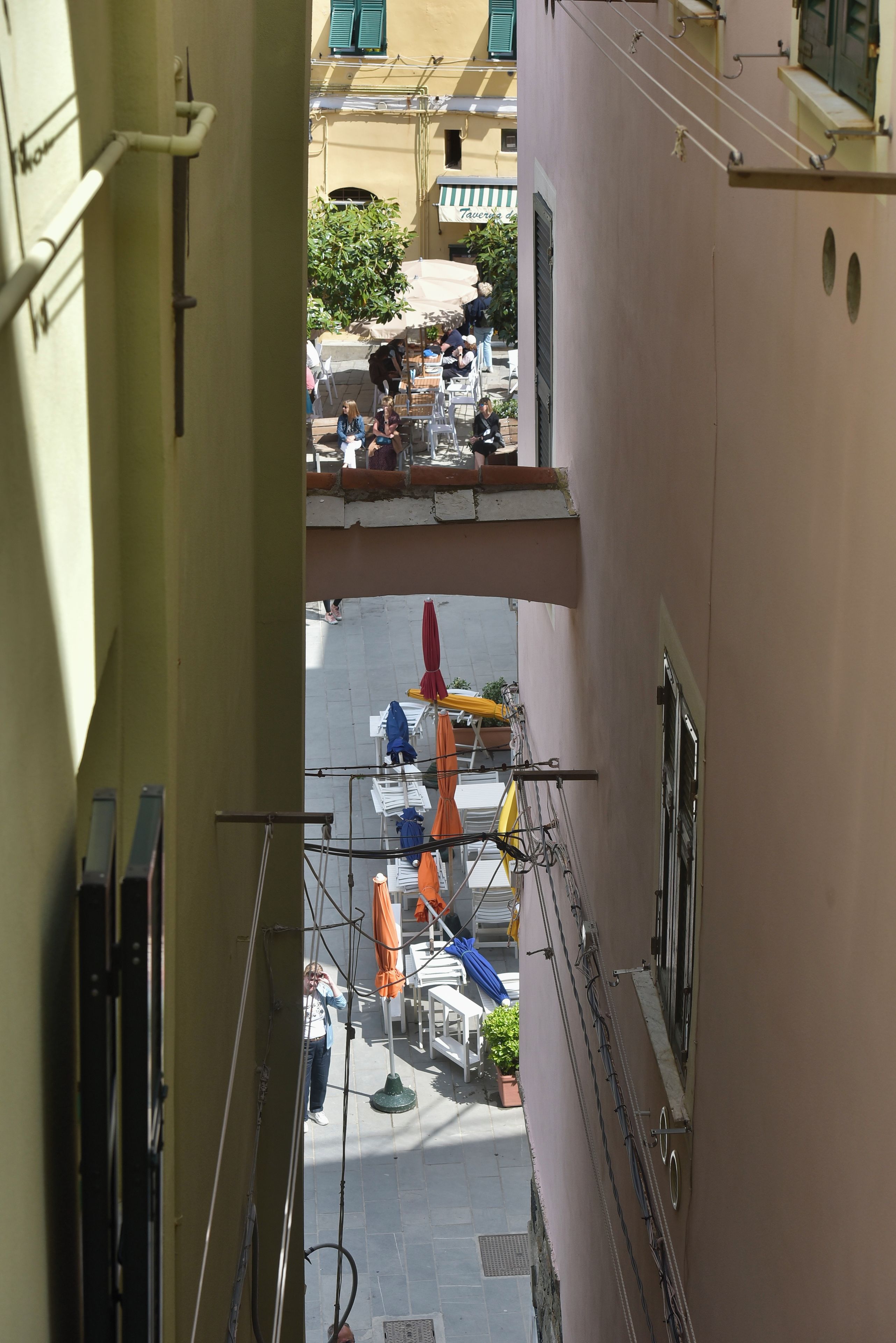 Un estrecho callejón flanqueado por edificios, con mesas al aire libre y sombrillas.