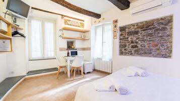 Un dormitorio con una cama, un escritorio y una computadora. Hay toallas sobre la cama y una ventana con cortinas.