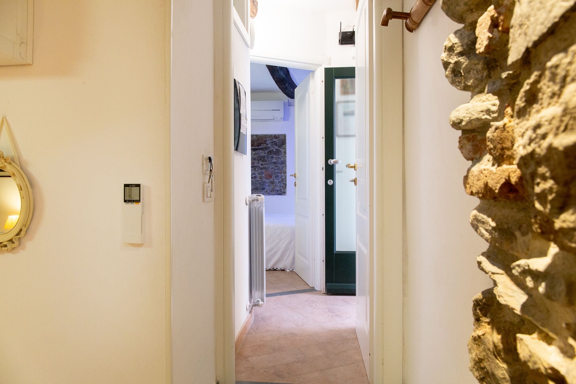 A narrow hallway with a stone wall on the right, a white door at the end, and a radiator on the left.