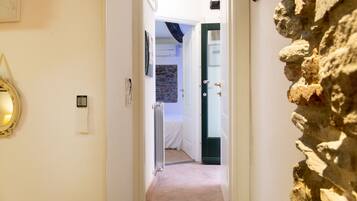 A narrow hallway with a stone wall on the right, a white door at the end, and a radiator on the left.