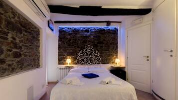 A bedroom with a stone wall, a bed with white linens, two bedside tables with lamps, and a door.