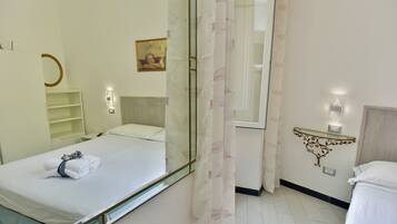 Habitación de hotel con cama, mesita de noche, espejo, estante en la pared y ventana con cortina.