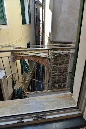 Une fenêtre ornée d’un garde-corps en métal donnant sur une ruelle étroite bordée d’immeubles.