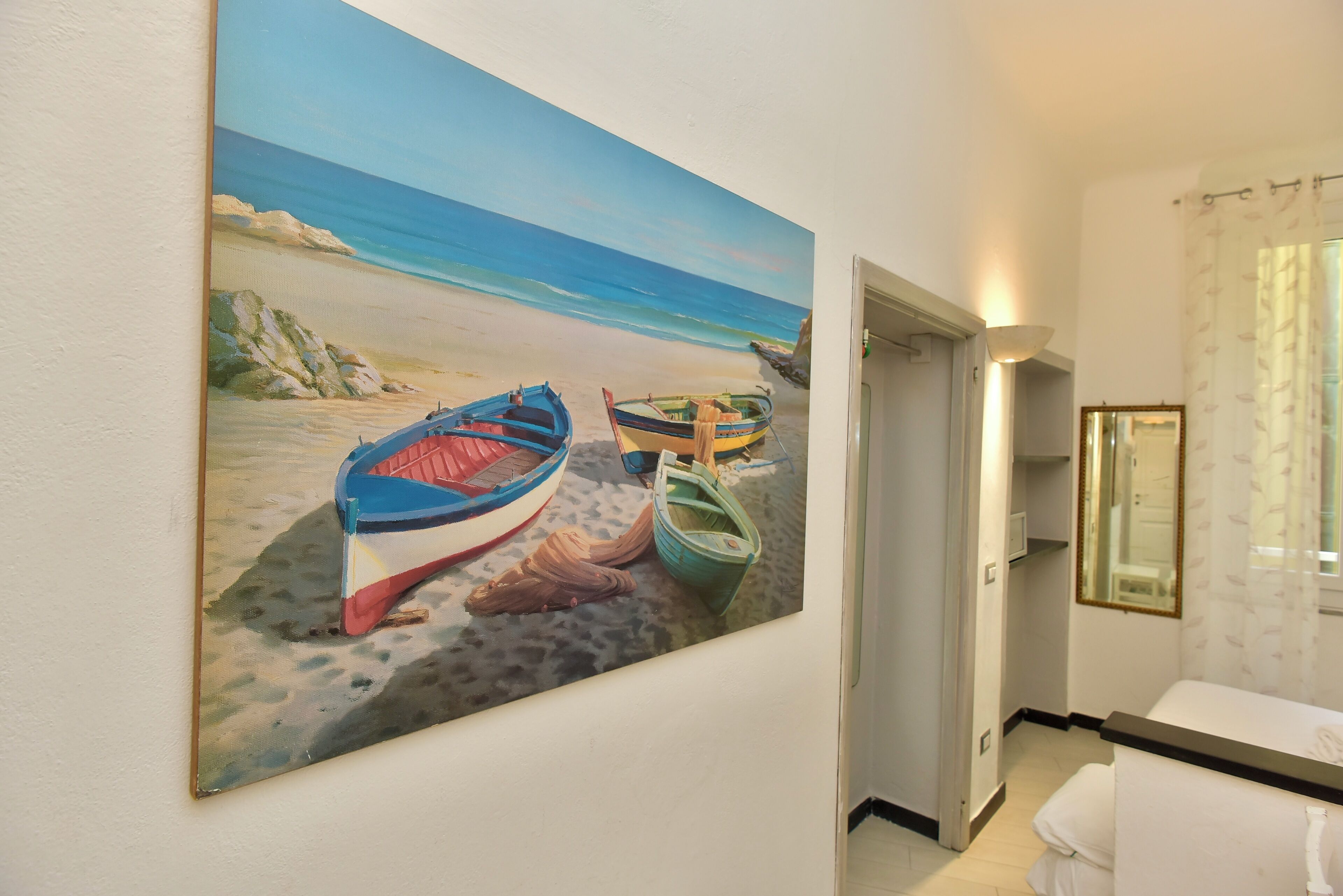A hallway with a painting of boats on a beach, a bathroom with a mirror, and a door leading to another room.